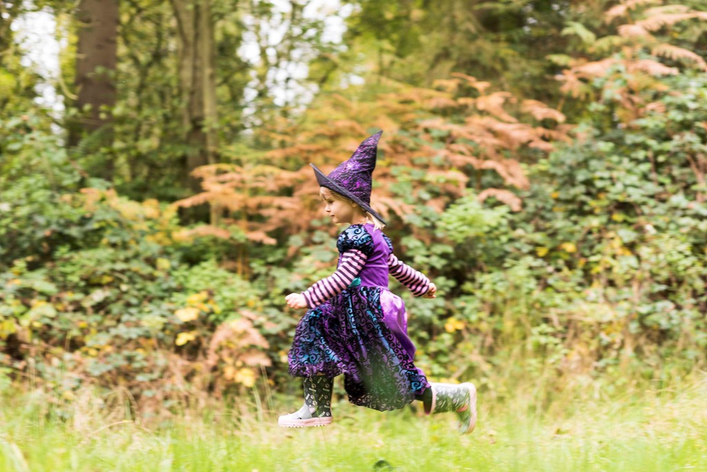 a young girl in a witches costume playing in the forest